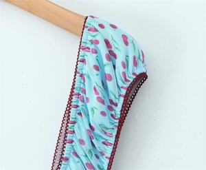 Dettaglio di tessuto floreale azzurro con stampa di ciliegie e bordo in pizzo rosso