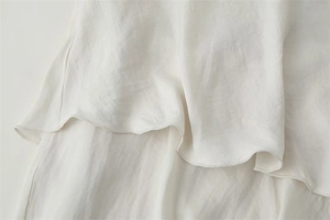 Detail eines weißen Lagenkleid-Saums aus seidig glänzendem Stoff mit feiner Rollsaumnaht