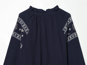 Detail of bohemian floral embroidery and ruffled collar on navy blue cotton blouse