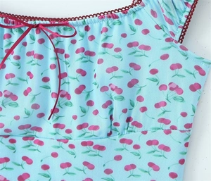 Dettaglio dello scollo con stampa ciliegia su mesh, bordo in pizzo e piccolo fiocco in seta rossa