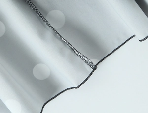 Détail du tissu à pois gris montrant les coutures surjetées noires et la texture fine