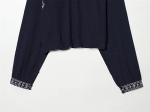 Detailed close-up of dark blue crinkled fabric with white ethnic embroidery on sleeves