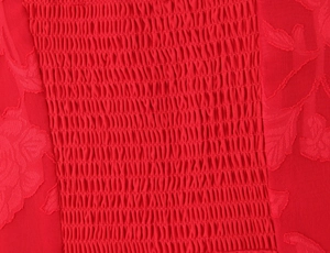 Detailed macro view of red smocking fabric with delicate floral embroidery texture
