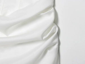 Detailopname van de witte geweven stoftextuur en vouwen van een midi-vestjurk