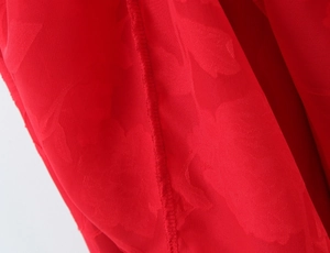 Detailed macro view of red chiffon floral jacquard fabric and clean overlock stitching seam