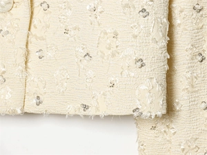 Macro detail of textured tweed fabric with 3D floral embroidery, sequins and pearls