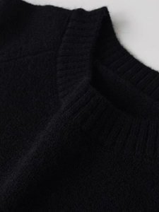 Dettaglio della trama a maglia a coste fitte e del tessuto morbido su un maglione nero a lupetto