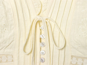 Détails du col V, boutons nacrés et broderie florale sur blouse en coton et lin crème