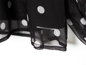 Detailed close-up of sheer black chiffon fabric with white polka dots and fine hem stitching