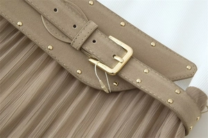 Détail d'une robe plissée kaki avec ceinture à clous dorés et boucle métallique