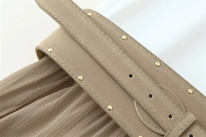 Détail d'une jupe plissée kaki avec large ceinture et rivets métalliques dorés