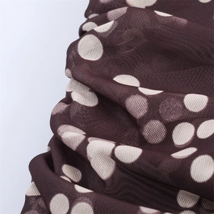 Detailed close-up of ruched sheer mesh fabric with polka dot pattern on a brown dress