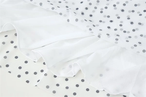 Detail of white polka dot mesh fabric with double-layered hem and ruffled edge finish