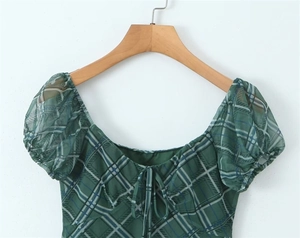 Détail d'une robe à carreaux verts avec encolure carrée à cordon et manches bouffantes