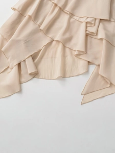 Close-up of layered ruffle hem on apricot asymmetrical mid-waist skirt with silky fabric