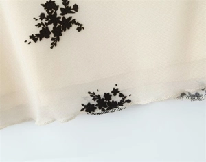 Detailed view of semi-transparent mesh fabric with black floral flocking and rolled hem edge