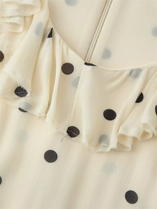 Détail du col en V avec volants et pois noirs sur un tissu en mousseline de couleur crème