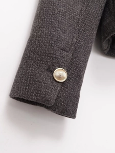 Detail of golden striped button on dark grey tweed fabric sleeve of the women's blazer