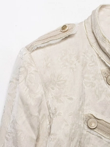 Detail of jacquard fabric texture with gold crest button and epaulet on a cream jacket