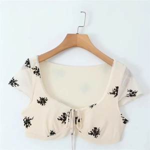 Short cream floral blouse with tie-front detail and bell sleeves on a wooden hanger