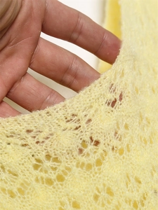 Close-up of bright yellow floral crochet knit fabric with mohair-like fuzzy texture