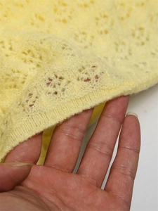 Macro detail of pale yellow openwork crochet knit fabric showing floral geometric patterns