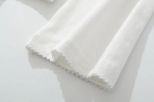 Detail of white cotton knit top featuring reinforced double stitching and wavy lace trim