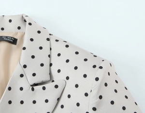Dettaglio colletto blazer a pois con etichetta taglia S su tessuto beige