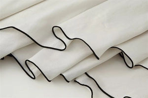 Detail shot of white fabric featuring elegant black wood ear edge stitching and silky texture