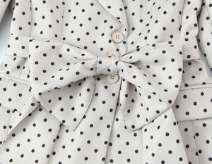 Dettaglio del fiocco in vita e bottoni sul blazer bianco a pois per donna