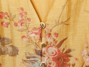Macro shot of V-neckline featuring rose-embossed buttons on floral print fabric