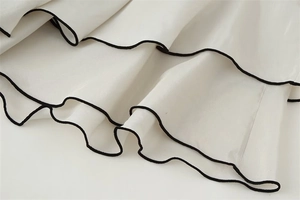Close-up of cream ruffled hem with black piping on elegant flowing skirt fabric