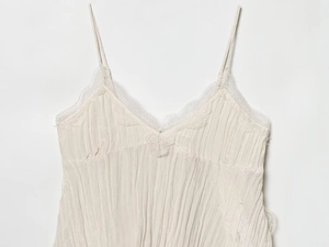 Detail of V-neck lace trim and pleated texture on an off-white camisole top