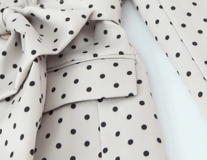 Dettaglio del blazer a pois con cintura in vita e tasca a pattina color crema