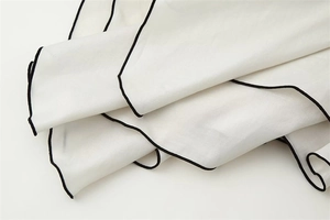 Macro shot of white lightweight fabric with fine black hemmed edges and subtle textures