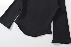 Detail of a black top with curved hem and delicate ruffle edges on soft fabric