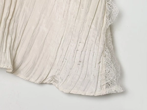 Detail view of cream vintage top featuring vertical pleated fabric and delicate lace trim edge