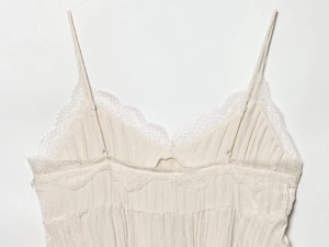 Detailed macro shot of vintage V-neck eyelash lace trim and pleated texture on a cream camisole