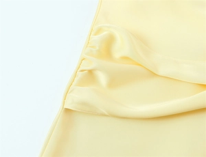 Dettaglio macro dell'abito in raso giallo chiaro arricciato con consistenza setosa del tessuto