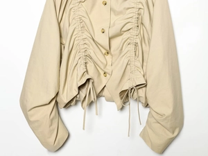 Detailed view of light khaki short jacket with unique front pleats and adjustable drawstrings