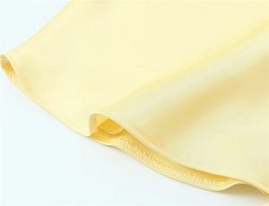 Dettaglio di abito in raso giallo chiaro con texture liscia e cuciture doppie di qualità