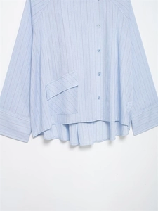 Detail of light blue striped shirt featuring a large diagonal pocket and button closure