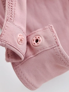 Gros plan détaillé du body rose montrant les boutons-pression en plastique et coutures