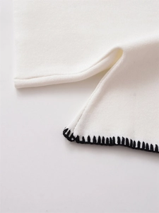 Detail shot of white knit fabric with elegant black blanket stitch finish on the edges
