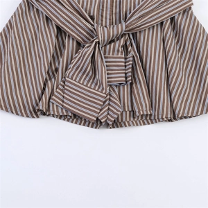 Detail of striped shorts with a tie-waist bow and button closure on brown fabric
