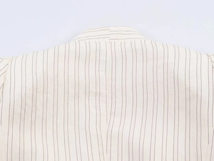 Macro detail of creamy blazer neckline featuring fine black vertical pinstripes and seams