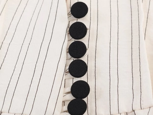 Detail of vertical black pinstripe fabric and round cloth-covered buttons on the blazer