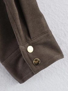 Detailed macro view of dark brown canvas jacket sleeve with two gold metal buttons