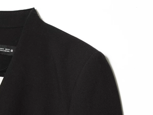 Détail de l'encolure du blazer noir montrant la texture du tissu et l'étiquette