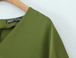Detail shot of olive green V-neck dress label showing brand Aveloria and size S